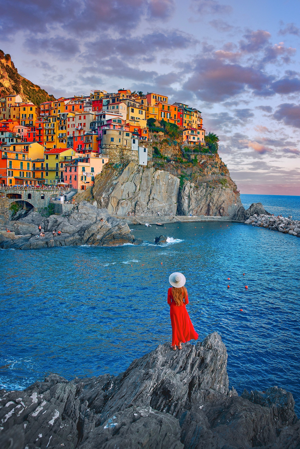 a girl in red sundress looking at the city of cinque terra