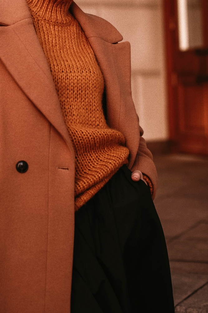 Female body in the orange warm knitting cozy sweater and long brown coat.