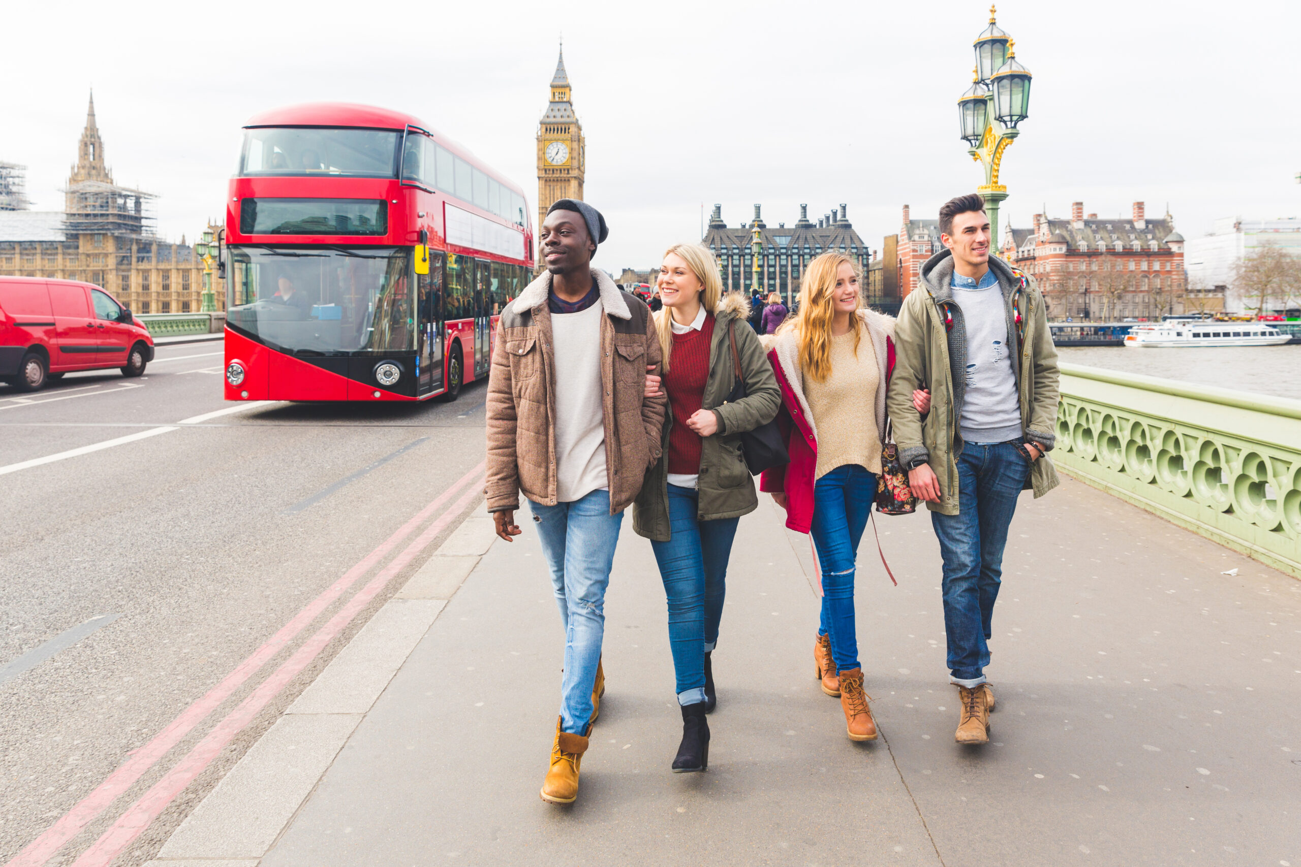  Mixed race people laughing and enjoying their time in the city. Big ben and double decker red bus on background. Dressed in winter clothes 