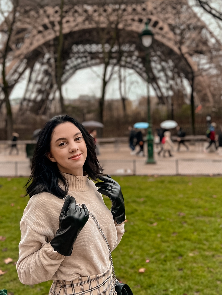 a woman standing in front of the eiffel tower in a chic sweater and leather gloves, she has on a cross body bag, what to wear in paris in february 