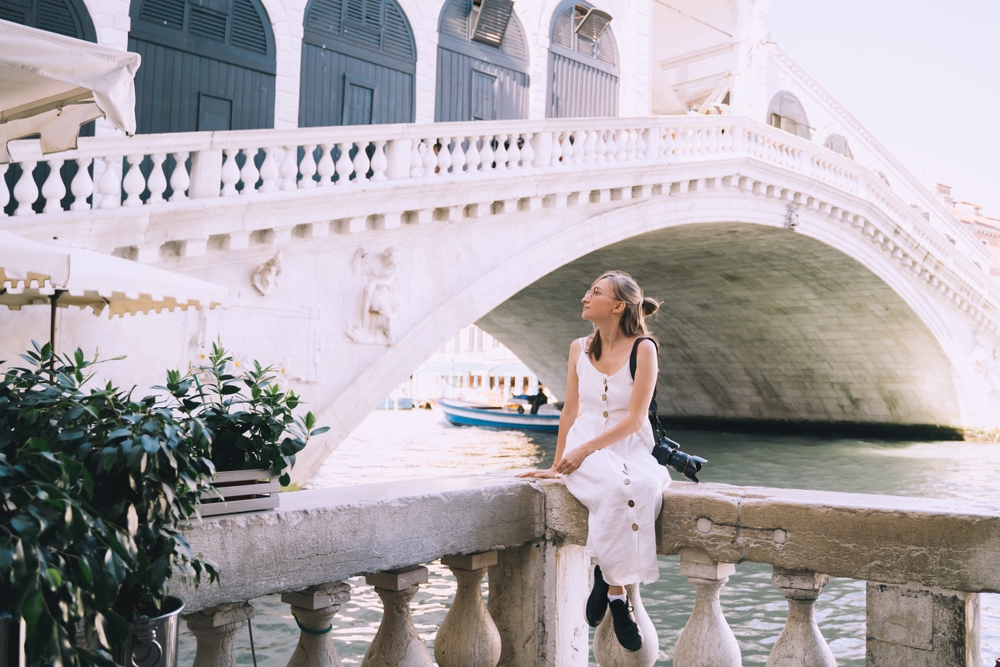  a girl I white dress and black sneakers sitting under bridge in Venice