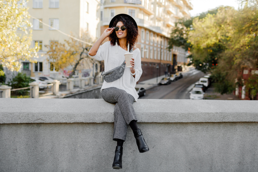 women in cropped trousers and hat sitting on bridge 