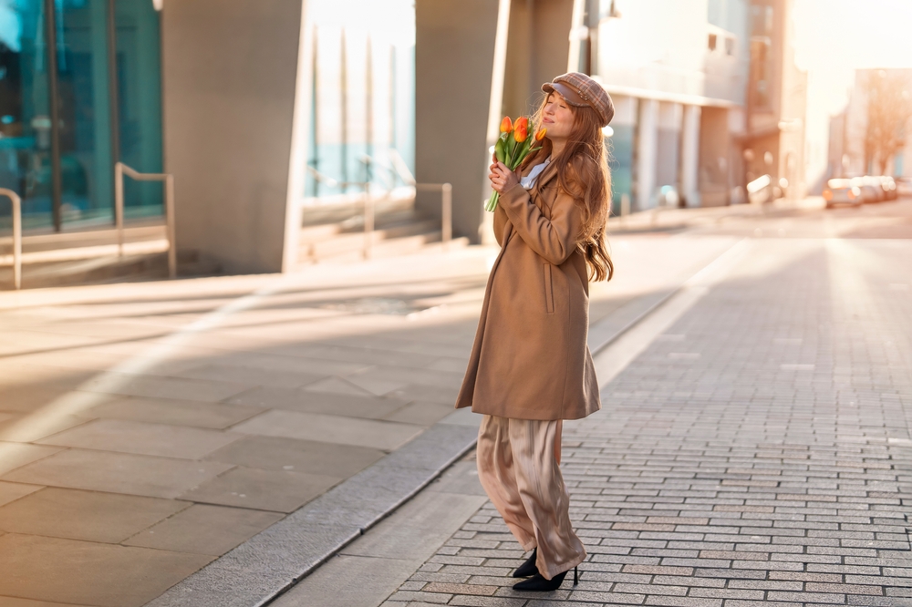 woman with flowers wearing a long coat and trousers in London  