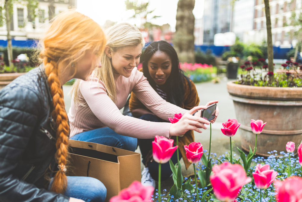 girls taking pictures of flowers. Article is about  what to wear in London in spring