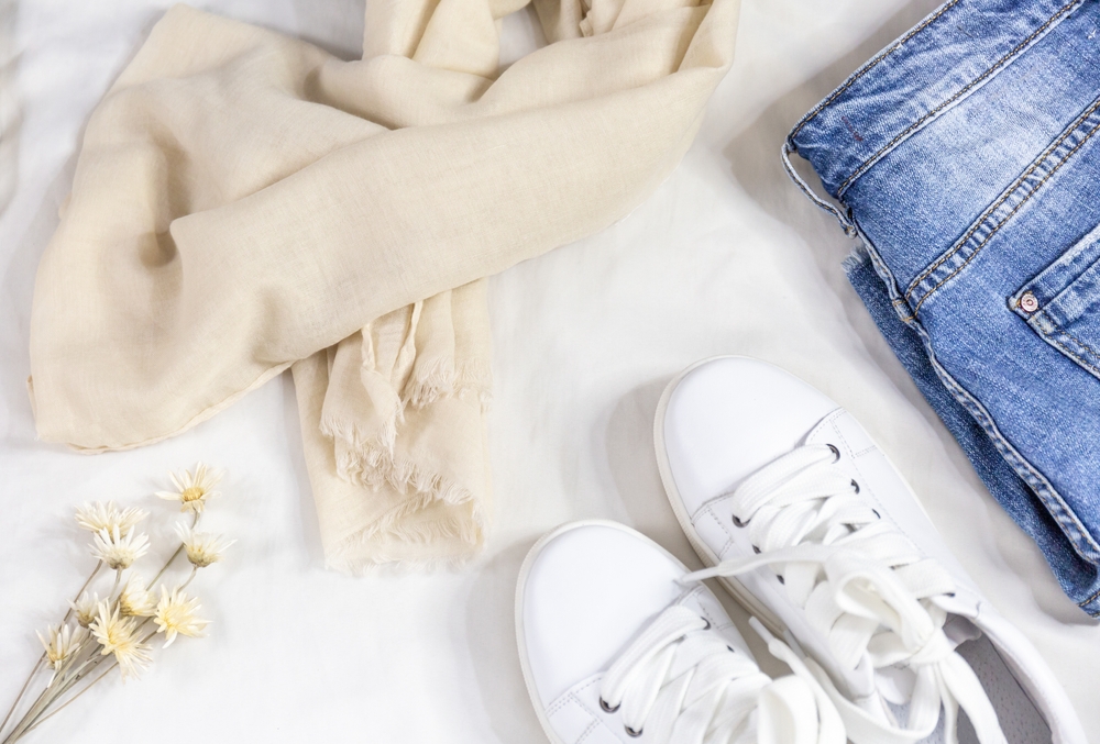 Flat lay image of a beige scarf, white sneakers, and denim shorts.