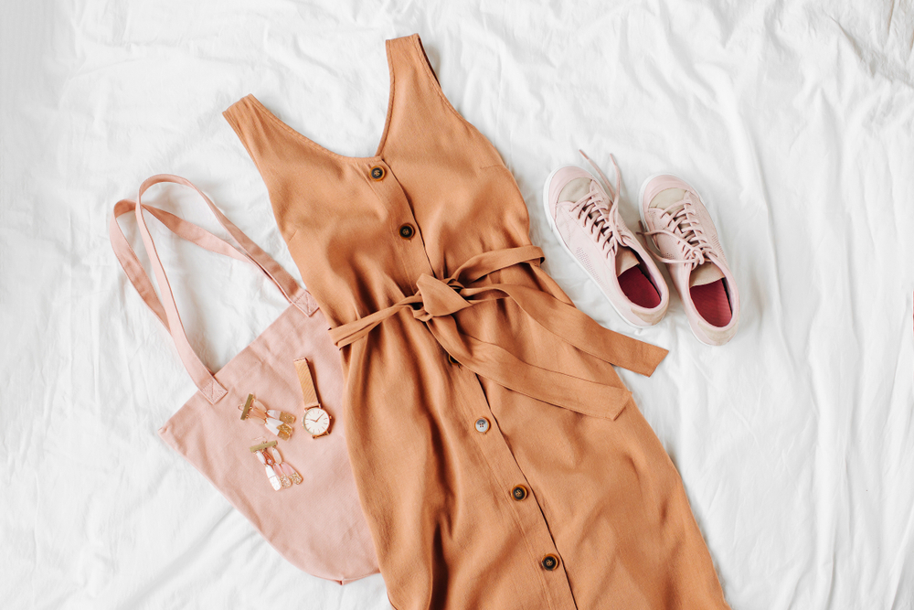 Flat lay image of a orange-beige dress pairs with soft pink sneakers and tote bag plus some accessories showcasing what to wear in London in Summer.