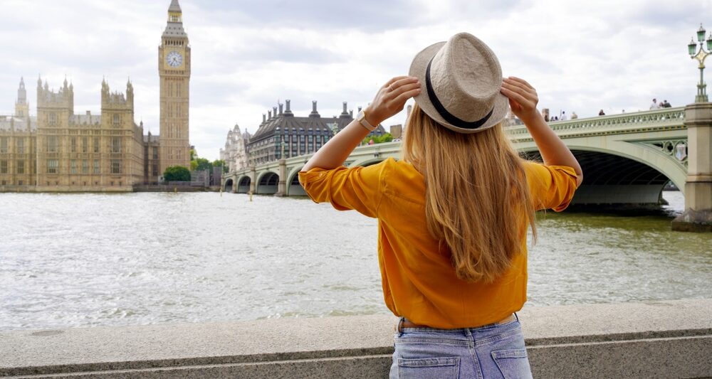 woman standing in front of big ben during london in summer wearing an orange top and blue jeans