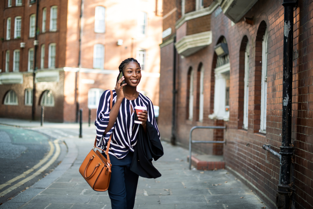 Smiling woman talking on the phone walking down the street wearing a striped shirt.