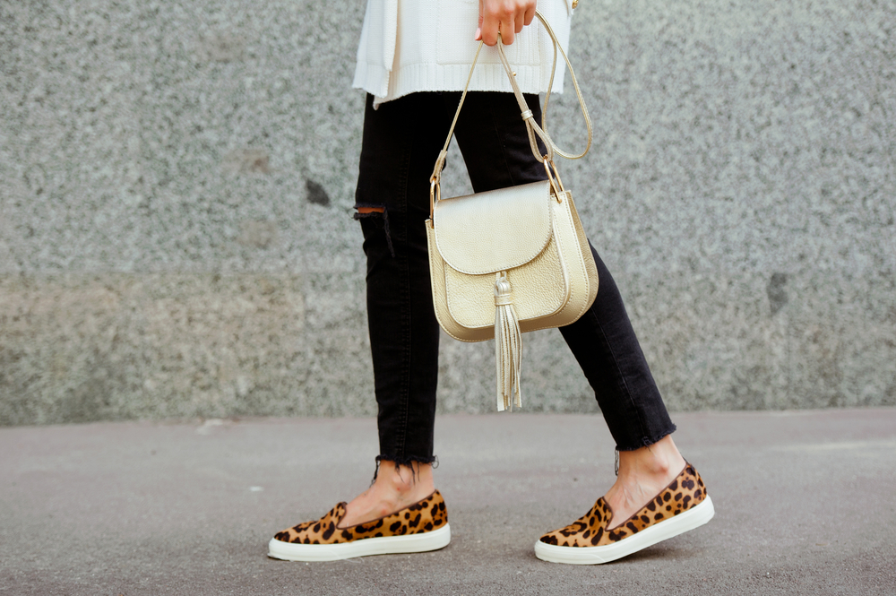 Waist down photo of a woman wearing black pants, leopard print flats and holding a purse, showing off good shoes for Paris Outfits in October.