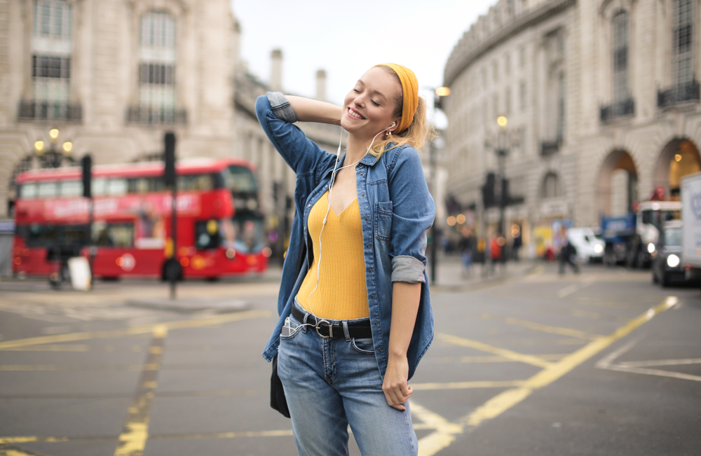 Woman listening to music in London while wearing a denim shirt over a yellow shirt.