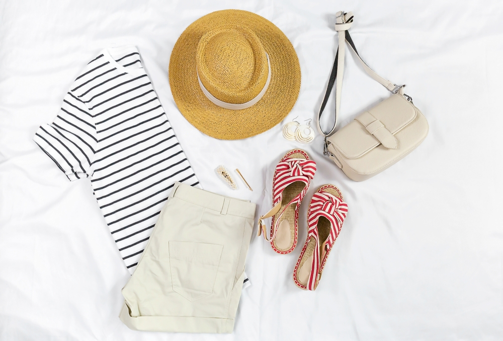 flatlay photo of a striped blouse, shorts, crossbody bag, hat, earrings, hair clips, and striped sandals