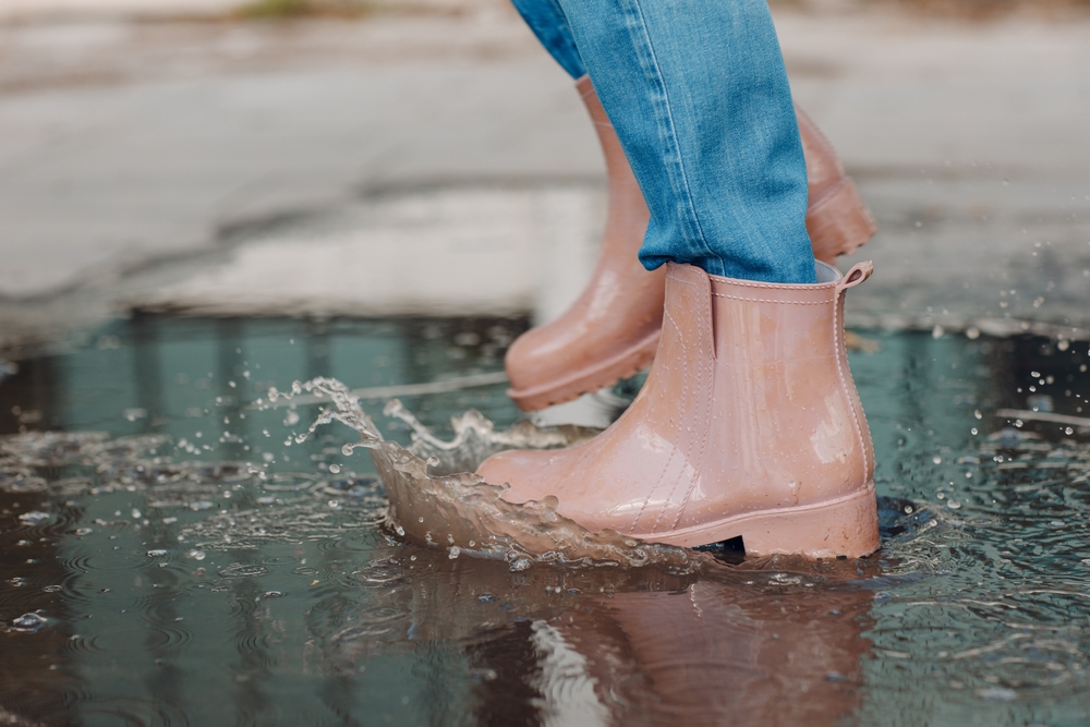 A pain of ankle, waterproof, rose pink boots splashes into a puddle on the streets. 