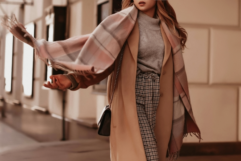 A women is fashionable in her plaid trousers, thick turtle neck, coat and plaid scarf. 