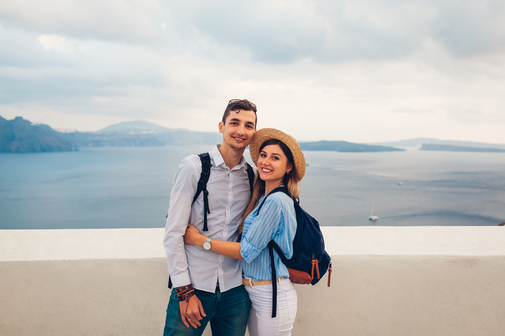 Couple wearing backpacks standing with the ocean behind them.