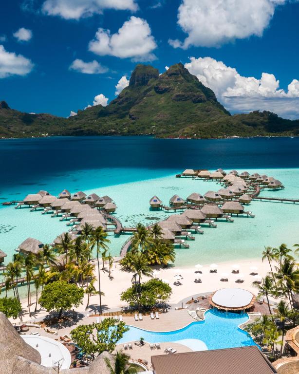 Picture of pool and beach with water bungalows and mountain in the background. 