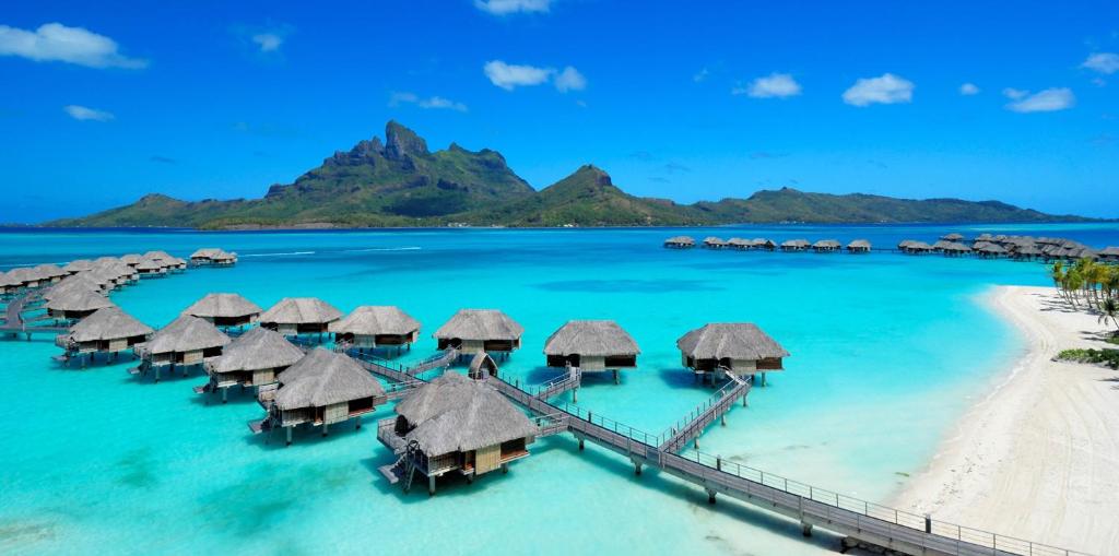 Overwater bungalows coming out from the beach with a mountain in the background.  