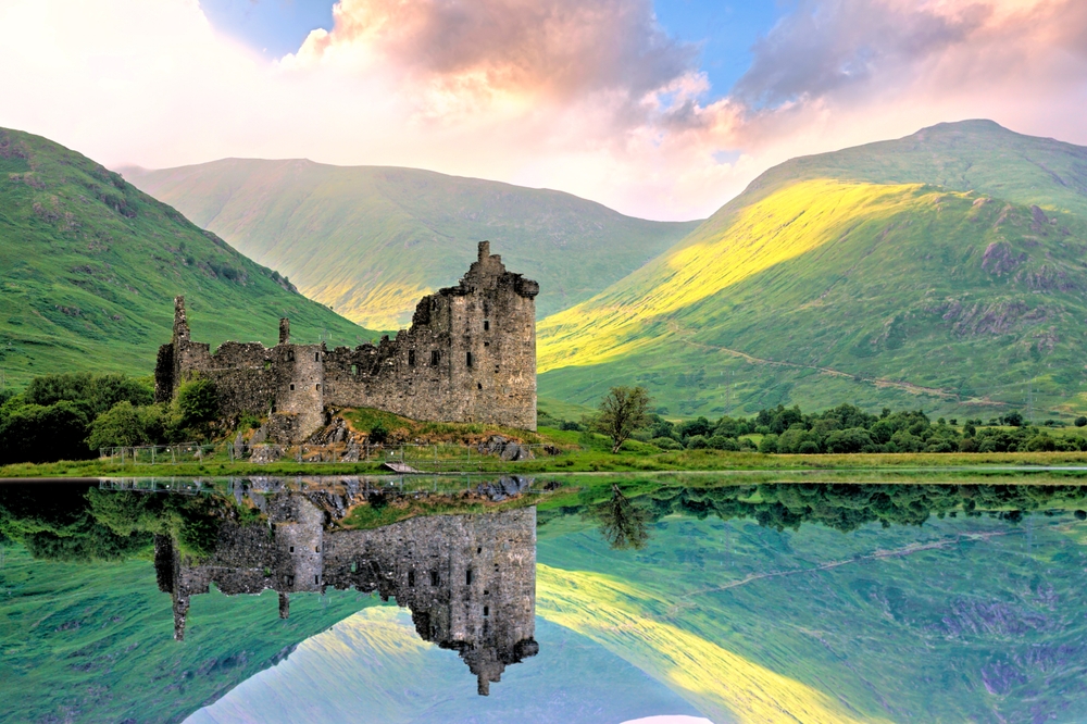 Scottish highlands with green rolling hills a lake and a ruined castle