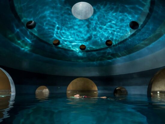 person floating on their back in a spa with giant gold balls around them and reflection of water on the celling in a round room