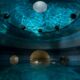 person floating on their back in a spa with giant gold balls around them and reflection of water on the celling in a round room