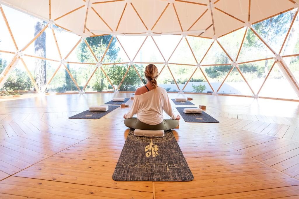 A women sitting crossed legs on a yoga mat in a dome clear building. 