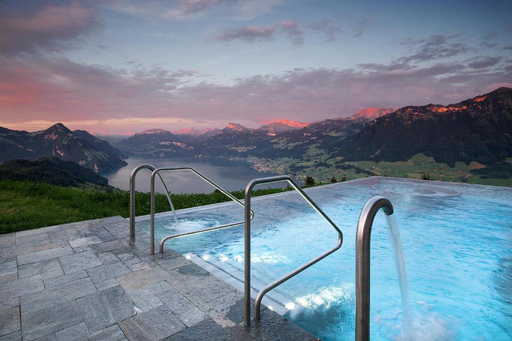 A picture of a hotel pool high up with a view of the mountains and lake. 