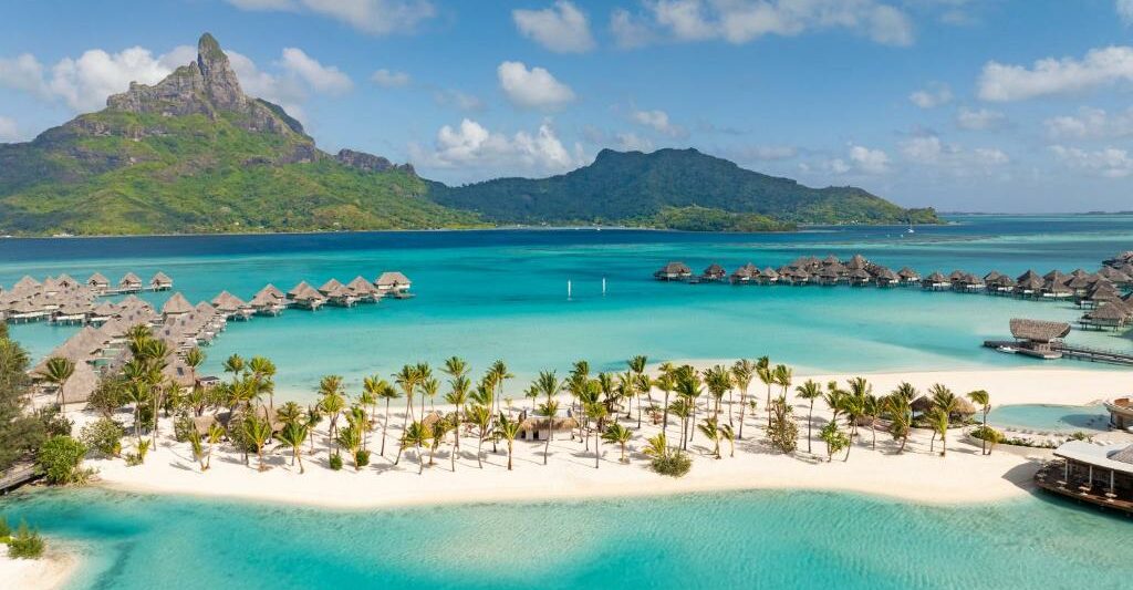 resort in bora bora with soft white sand and overwater bungalows in the background and a mountain