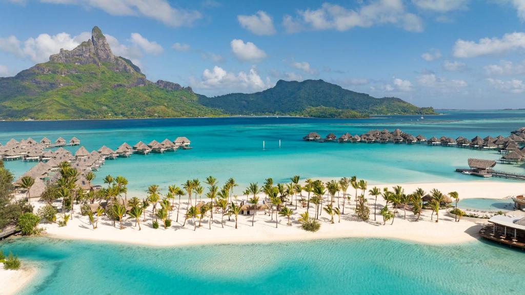 An island with a beach and palm trees and overwater bungalows and a mountain in the background. One of the best resorts in Bora Bora