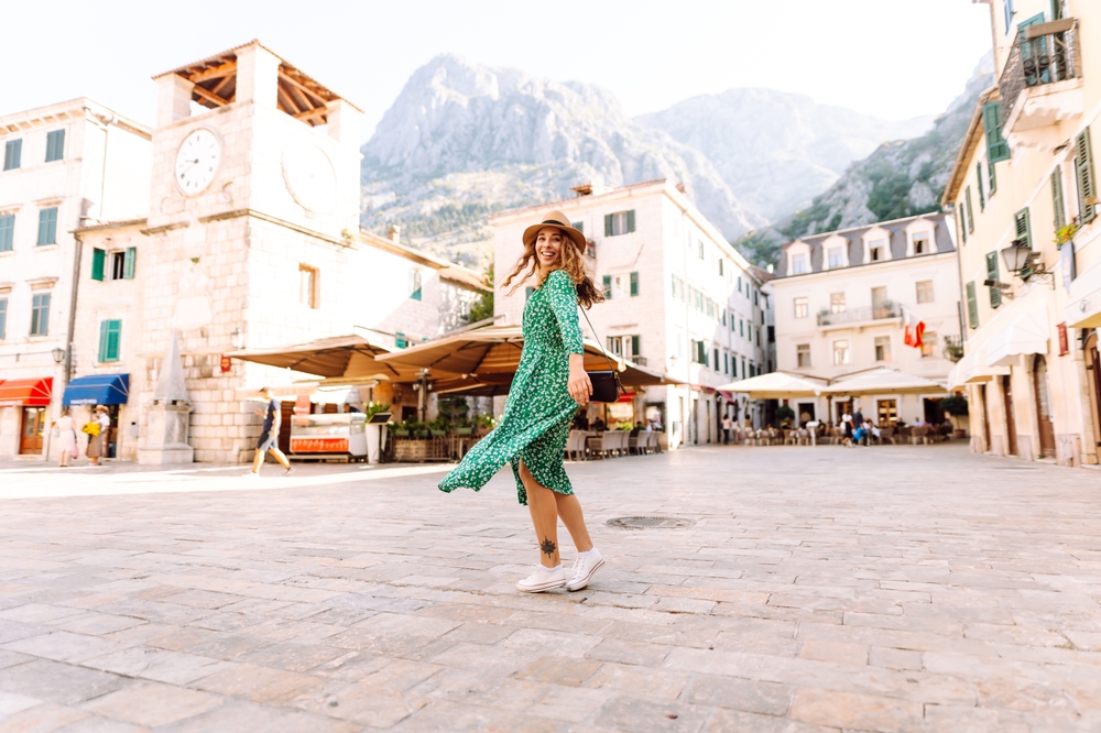 A woman in a green midi-skirt and white converse twirls in the middle of town square. 