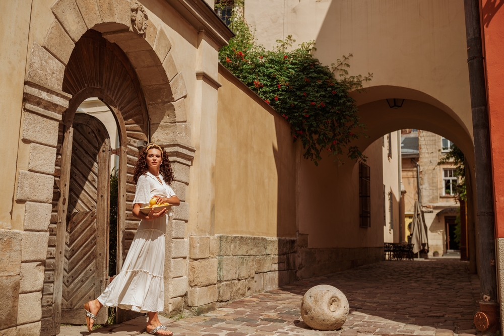 A woman sneaks into the alley of a European city in a maxi skirt and a matching flowing blouse. 