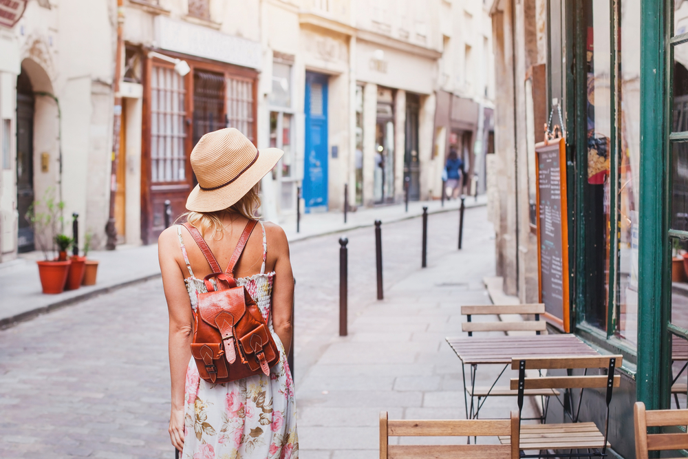  When wondering what to wear in the city in the summer, think comfort and breezy, like this woman did as she walks down the alleyway in Italy in a sundress, straw hat and with a leather backpack. 