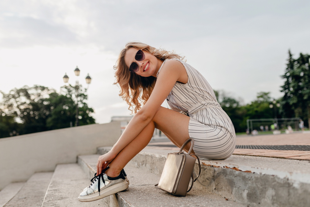 When wondering  what to wear in the city in the summer, channel this girl's outfit: she sits on a stairs in her comfortable sneakers and a romper that is striped and breezy. 