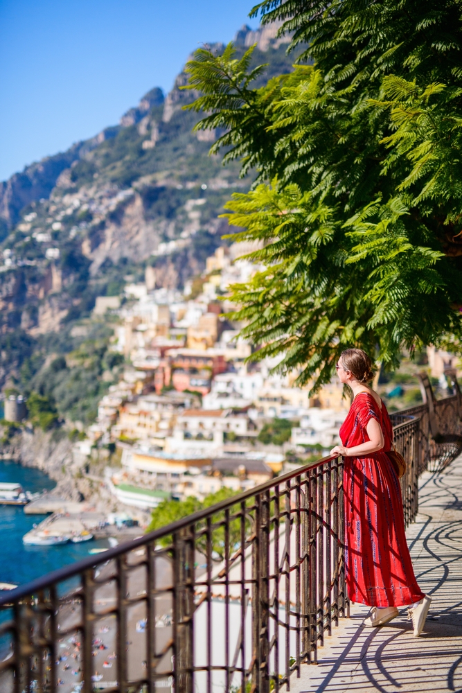 a flowy sundress in red with a. woman overlooking one of the towns on Amalfi is perfect summer outfit for what to wear on Amalfi Coast