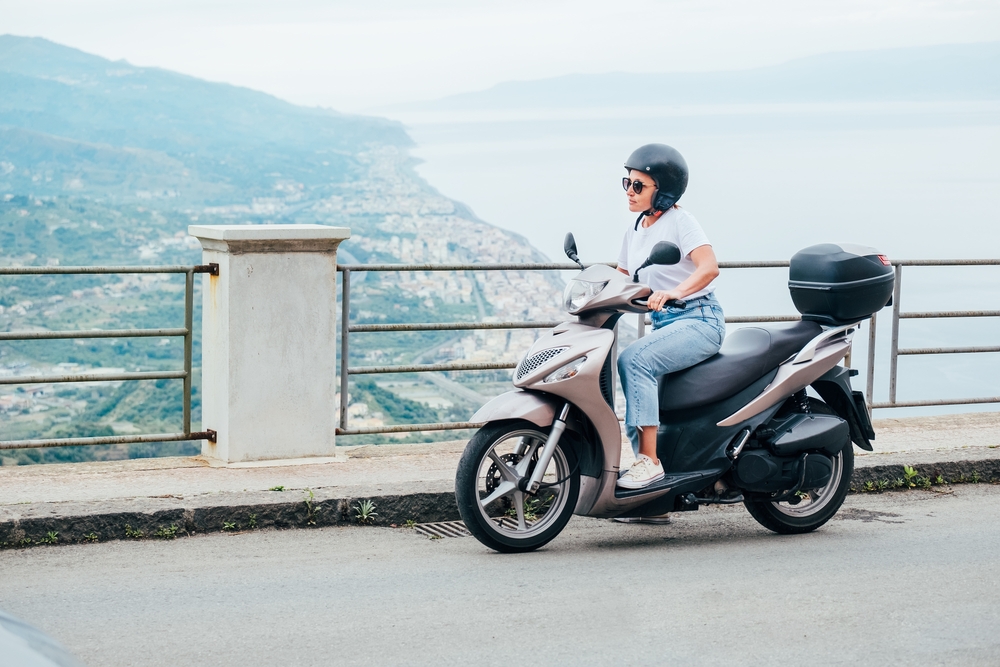 a woman in jeans and white shirt with sneakers on a vespa