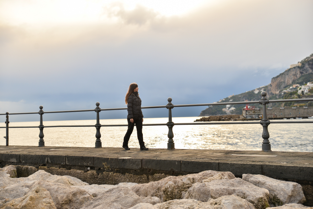 a woman walking along seaside village in winter with black puffer coat and black jeans with boots