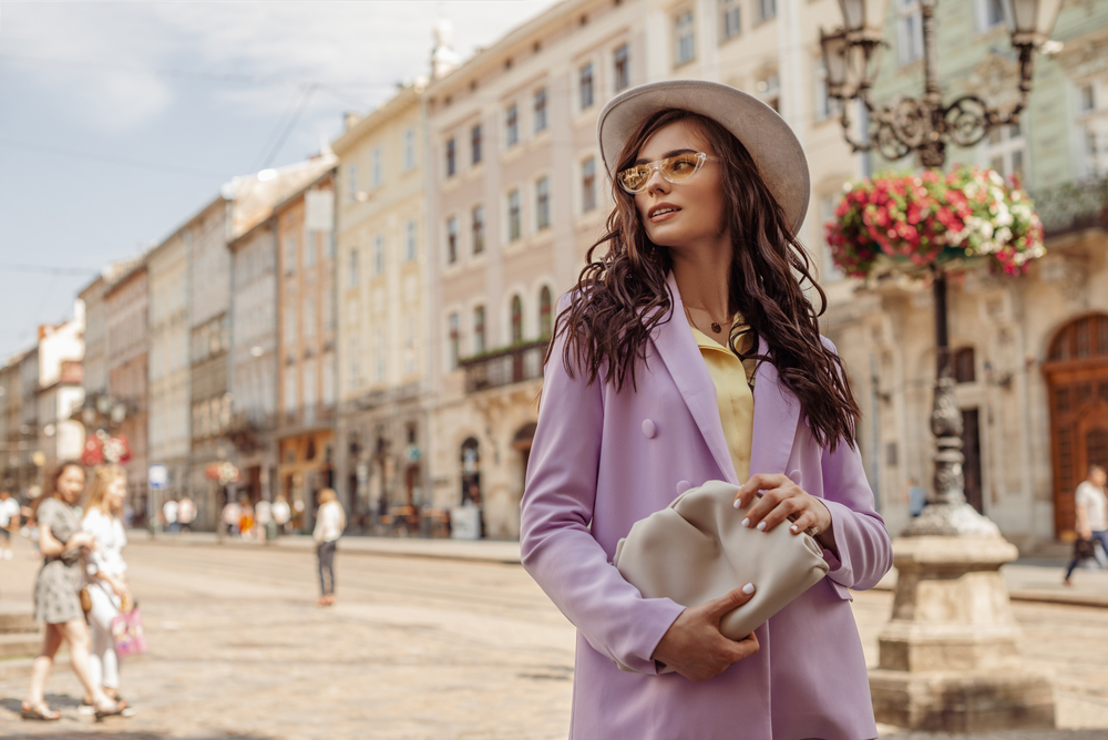 A woman in a purple trench coat and yellow blouse clutches a purse as she glances over her shoulder in the streets of Rome. 