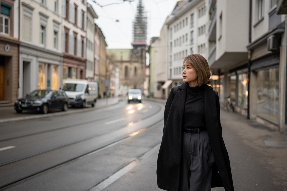 A woman walks down the streets of L London in a black trench coat, dark jeans and a dark shirt. 