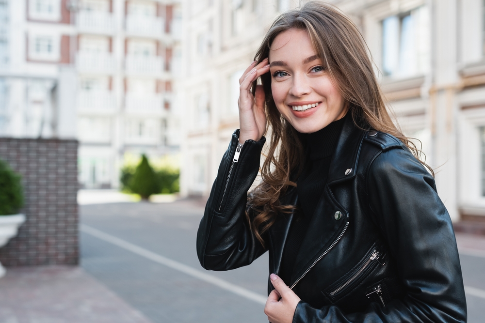 A woman smiles at the camera in Europe with a black leather jacket and a matching turtle neck underneath it. 