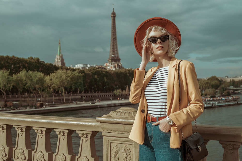 Sometimes wondering what to wear in Europe in spring is dependent on where you're going: this woman stands in front of the Eiffel Tower in a stripped shirt and blazer, perfect for Paris. 