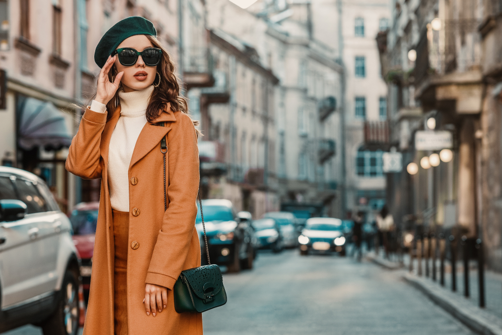 A woman pauses in European streets, confident that she knows what to wear in Europe in spring with her turtle neck, beret, trench coat and more. 