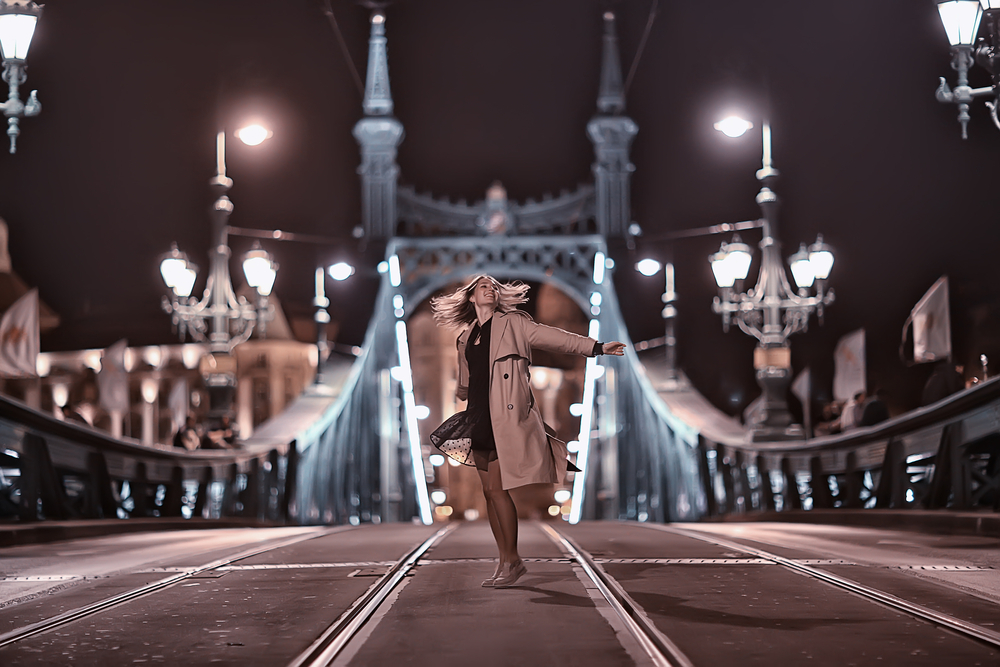 A woman dances on an empty tower bridge, her trench coat, black dress and slip on shoes spinning with her. 