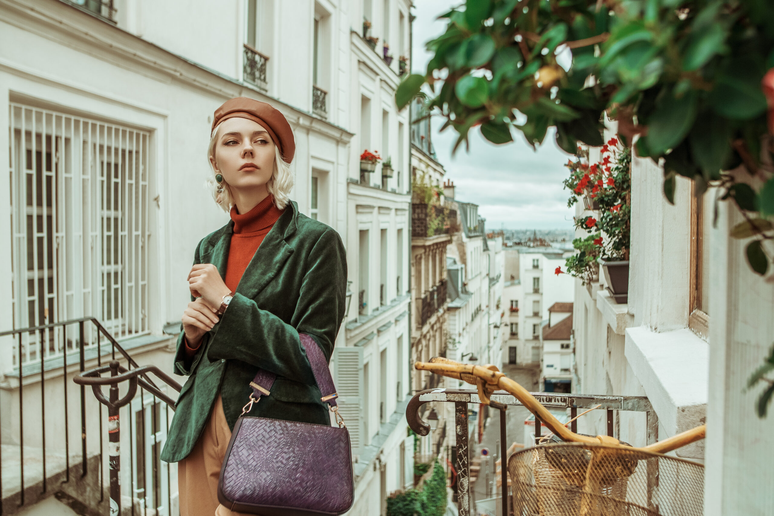 A woman is on the stairs wearing a green blazer, trousers, and a turtle neck, enjoying the scenery in Paris, not worrying about what to wear in Paris in fall. 