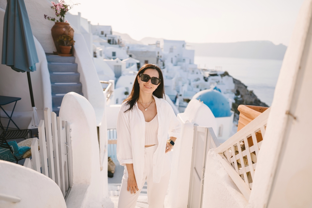 A white button down, crop top, and linen pants is the perfect outfit on this model as she stands on the stairs of the city, the blue and white buildings behind her. 