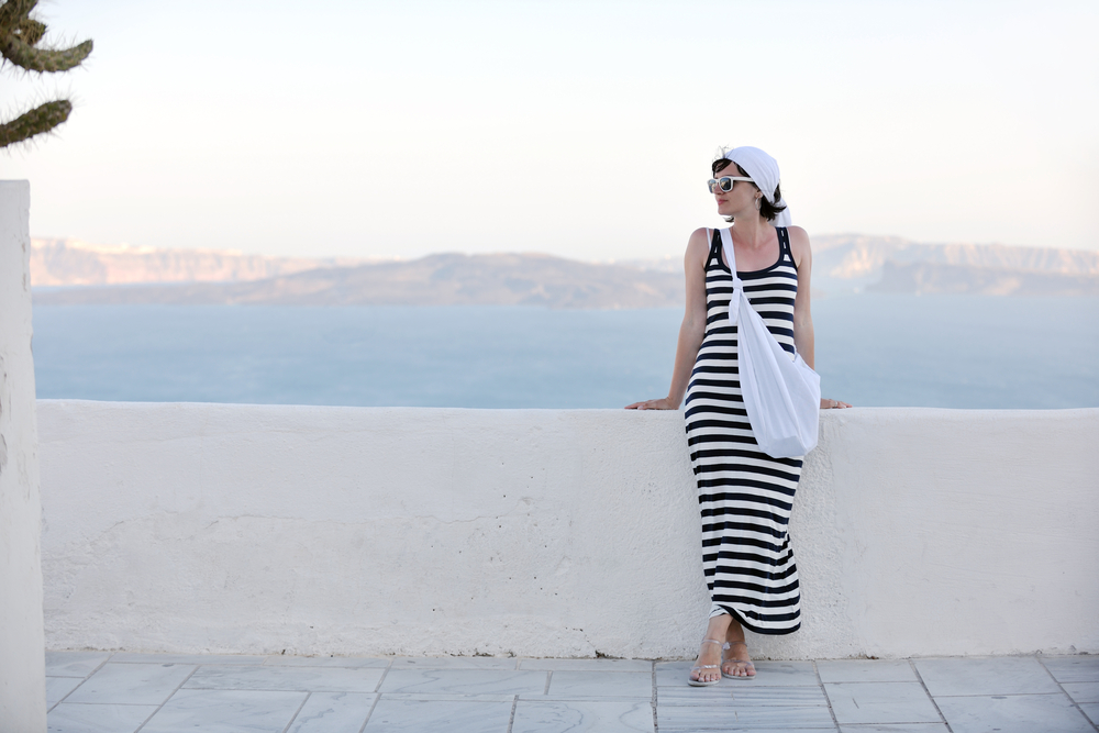 when considering what to wear in Santorini Greece, this woman opted in for a maxi dress that was on theme with nautical vibes: the stripes and white bag and white sandals have her at home. 