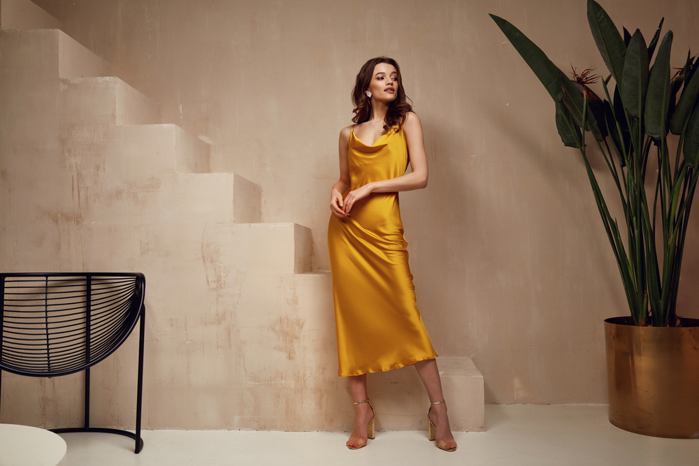 A woman in a golden, yellow, satin dress looks over her shoulder, exuding confidence on what to wear on a cruise since she has it ready for formal nightlife nights! 