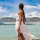 A woman in a skirt and tube top looks back at her cruise ship as it is docked, not worried about what to wear on a cruise because she is comfortable and cute!!