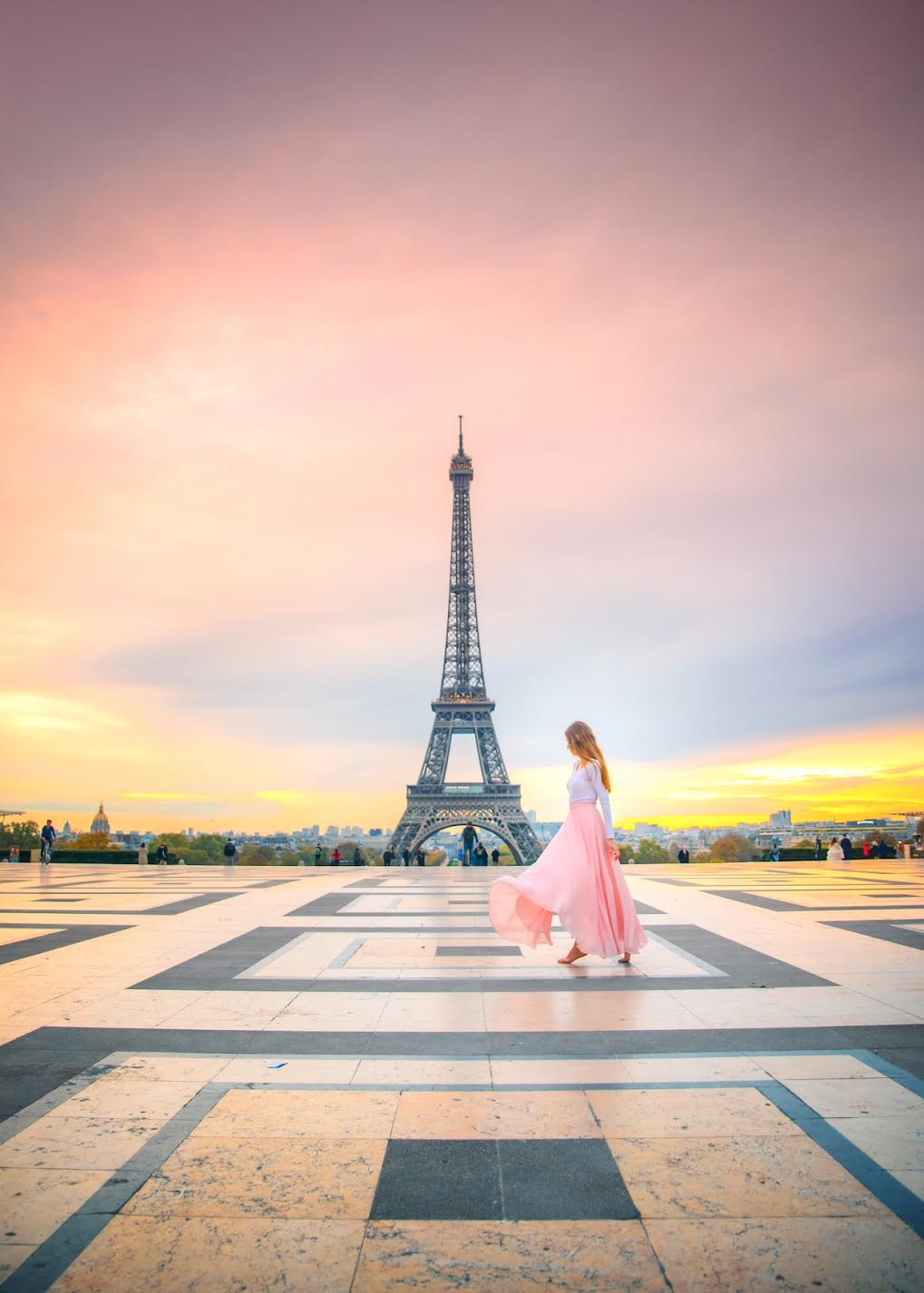 eiffel tower in paris in the background, a woman in a long skirt is standing in front of it and the wind is blowing the skirt around beautifully 