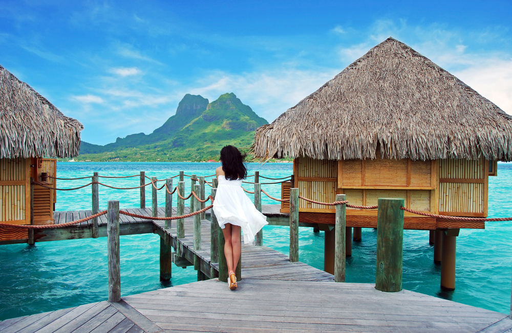 one of the best bora bora outfits, a short strapless flowy dress worn by a woman standing on a wooden walk way over the water 