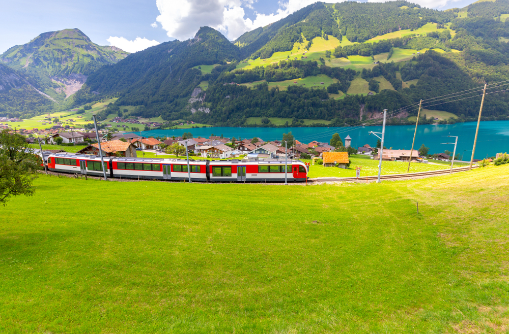 a train passing through the green foothills and a lake in Switzerland