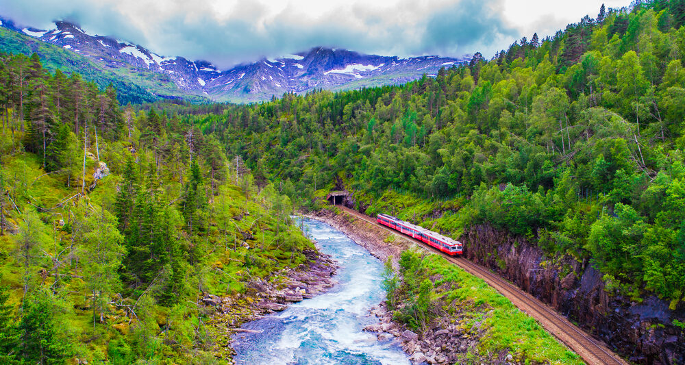 a train passing along Norway with mountain and river