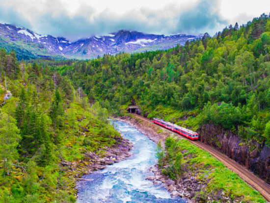 a train passing along Norway with mountain and river